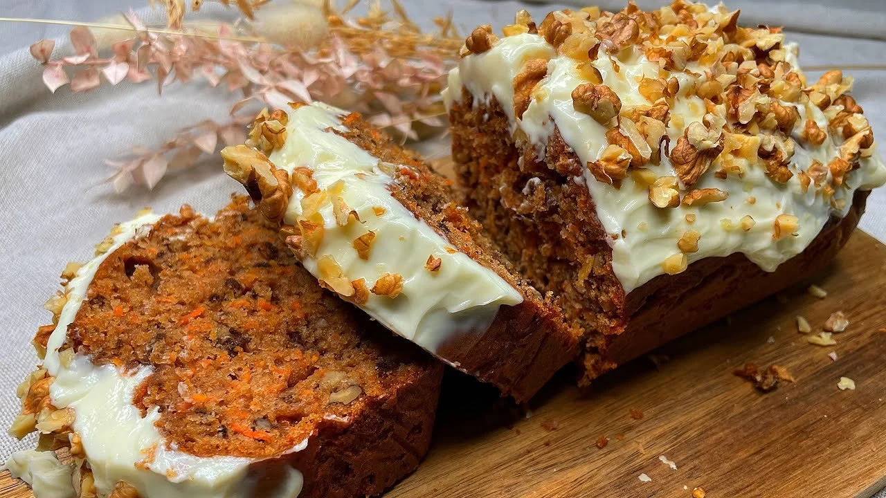 Finom karottenkuchen képe, sárgarépával és dús krémmel díszítve.